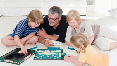 Isä pelaa lasten kanssa lattialla Scrabblea.
