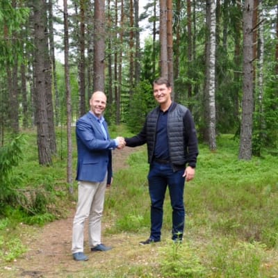 Två män står i en skogsdunge och skakar hand. Det är Sjundeås tekniska direktör Markus Moisio och Oskari Seppelvirta från byggbolaget Ki Oy Rovaniemen Sarkatupa.