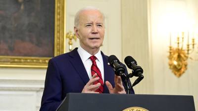 Joe Biden står vid ett talarpodium med presidentens sigill och ser rätt glad ut. Han gestikulerar med händerna.