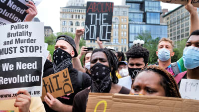 Demonstranter som protesterar mot polisbrutalitet håller i skyltar och har munskydd på sig i USA.