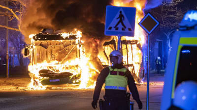 Polis i kravallutrustning står framför en brinnande bil i Malmö