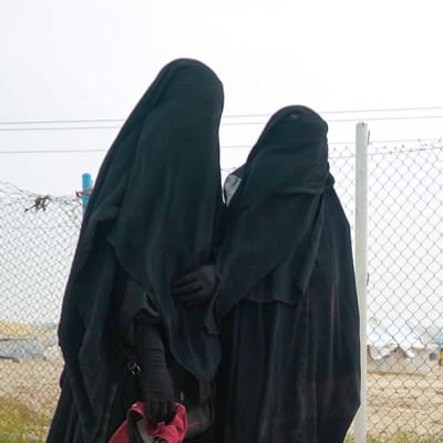 Två kvinnor står framför ett stängsel på lägret al-Hol i Syrien.