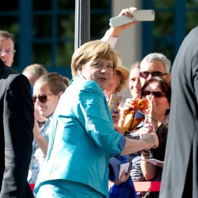 Juhla-asuiset Angela Merkel ja Joachim Sauer nimikirjoituksia pyytävän ja valokuvaavan katsojajoukon keskellä Bayreuthin oopperajuhlilla 25.7.2015. 