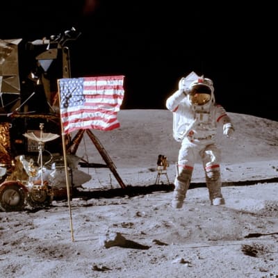 Astronautin takana lipputanko lippuineen sekä astronauttien kuukärry. 