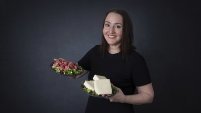 En kvinna ler glatt och serverar en tallrik med kallskurna köttprodukter och en tallrik med ost.