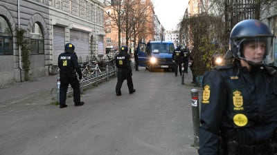 En handfull danska poliser i hjälm går mot en polisbil på en gata.