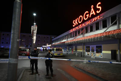 Två poliser står framför ett polistejp. I bakgrunden ett köpcentrum med texten Skogås centrum.