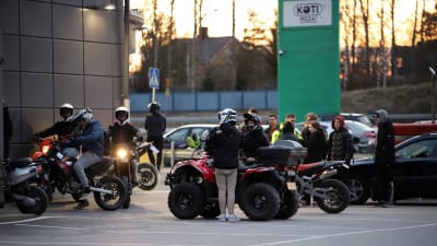 Ungdomar står med mopeder och fyrhjulingar på en parkering i kvällsljus.