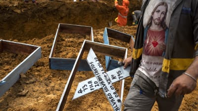 En gravgrävare står framför en massgrav med kors i handen