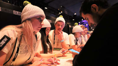 Vitklädda ungdomar vid en disk hjälper deltagare på Slush. 