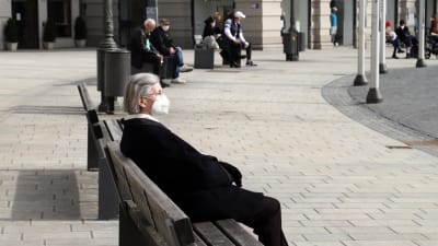 En dam med munskydd sitter på en bänk i staden Augsburg