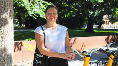 En kvinna i vit t-skjorta står med händerna på ett cykelstyre.