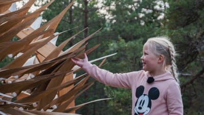Nellie Wallden koskettaa suurta, puusta tehtyä taideteosta, jossa on liikkuvia siipimäisiä ulokkeita.