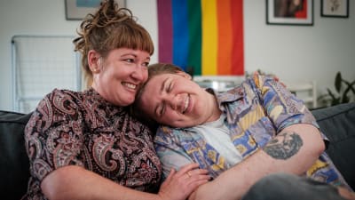en mamma kramar om sin son som är trans, de ler och sitter på soffan tillsammans.
