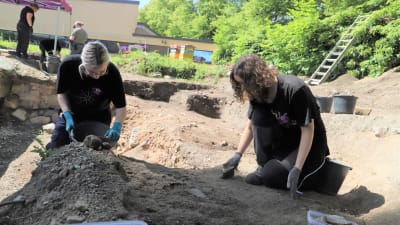 Två praktikanter gräver efter arkeologiska föremål.