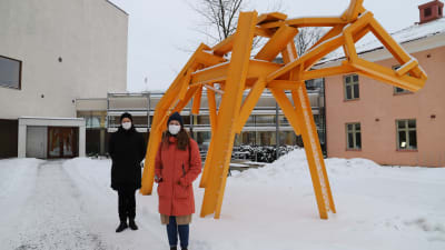 Andrea Södergård och Minna Hemgård står bredvid ett konstverk som föreställer en gul ko på Åbo stadsbiblioteks innergård. 