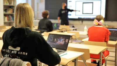 Abiturienter sitter i ett klassrum och lyssnar på en lärare som pekar på något.