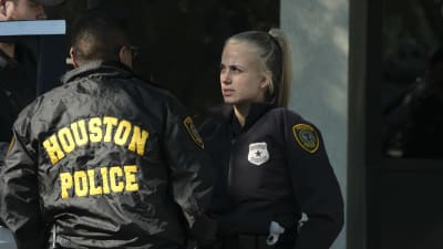 Två poliser, men mörkhårig man och en blond kvinna, talar med varandra. Mannen har ryggen vänd mot kameran. På hans rygg står Houston police.