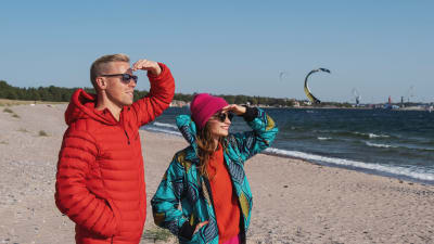 Egenandin juontajat Nicke Aldén ja Hannamari Hoikkala katselevat aurinkoisena päivänä Tulliniemen rannan purje- ja leijalautailijoita.
