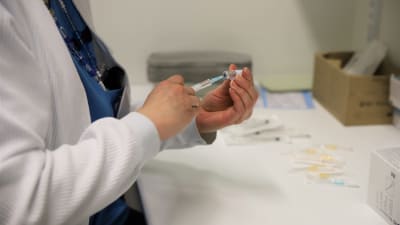 En skötare fyller en spruta med coronavaccin. 