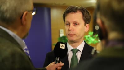 En man i kostym och grön slips intervjuas för TV. 