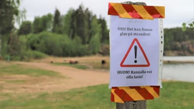 Varningsskylt vid Bläsnäs badstrand. Texten lyder: OBS! Det kan finnas glas på stranden!