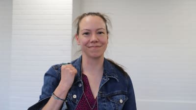 Kvinna med jeans-jacka ler in i kamera.