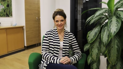 Mikaela Sundqvist  sitter i en grön stol bredvid en grön växt i ett kontorsutrymme.
