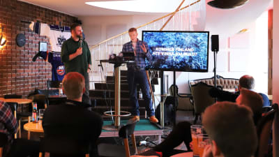 Två män diskuterar framför en livepublik.