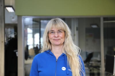 En kvinna med långt ljust hår, glasögon och en klarblå blus.