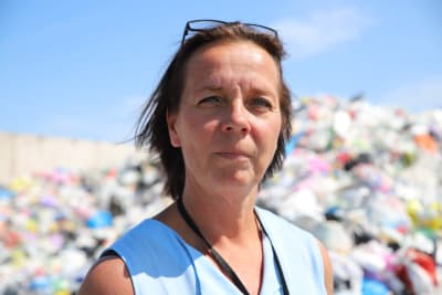 Bild av en kvinna som står framför högar med plastsopor. 