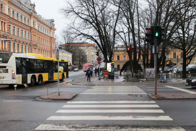 En skyddsväg med grönt ljus och en gul buss i bakgrunden.