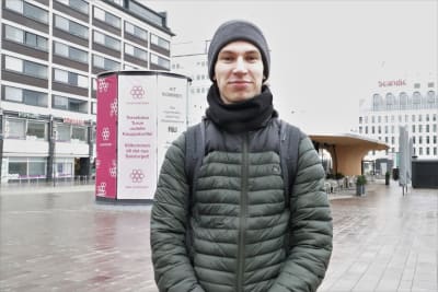 En ung man med grå mössa och grön rock ser in i kameran.