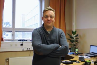 En man med kort hår och grå tröja ler och ser in i kameran.