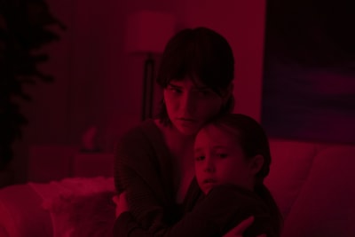 En tonårsflicka håller sin lillasyster i famnen i ett rum som badar i ett rött sken.