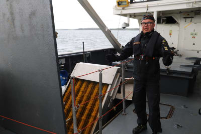 Em man klädd i sjöbevakningens uniform står bredvid en oljebekämpningsapparat. 