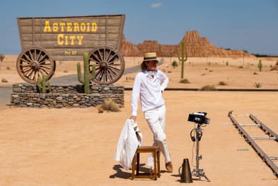 Regissören Wes Anderson poserar i ett ökenlandskap framför en vagn på vilken man kan läsa Asteroid City.