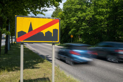 Ett trafikmärke som visar att tätort upphör syns i förgrunden, vid sidan av det två bilar som är fotade med rörelseoskärpa.
