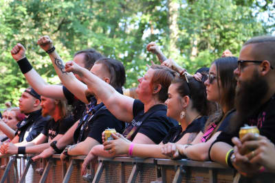 Personer i svarta T-tröjor står längst fram vid scenen på en metallfestival, lyssnar på musiken och håller upp sin ena hand som är knuten.