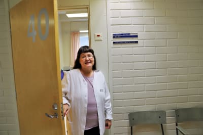 Terhi Vörlund-Wallenius håller i en dörr. Dörren går till hennes mottagningsrum på Åbo hälsocentral. Bredvid dörren står en skylt med hennes namn på.