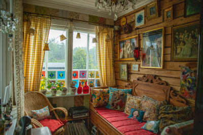 Tamburen med stockvägg, träsoffa med färgranna textiler och massa tavlor på väggen.