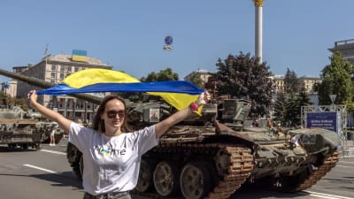 Kvinna håller upp ukrainsk flagga framför en beslagtagen rysk stridsvagn i Kiev.