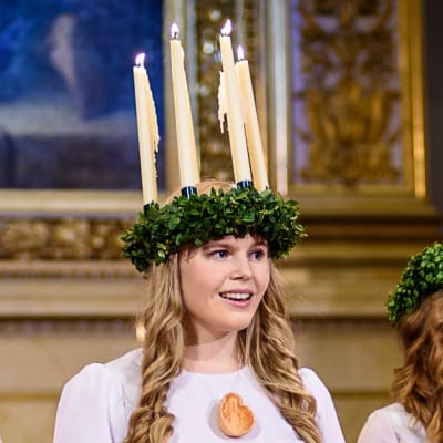 Finlands Lucia 2016 Ingrid Holm iklädd ljuskrona och vit luciadräkt med tärnor i Helsingfors domkyrka.