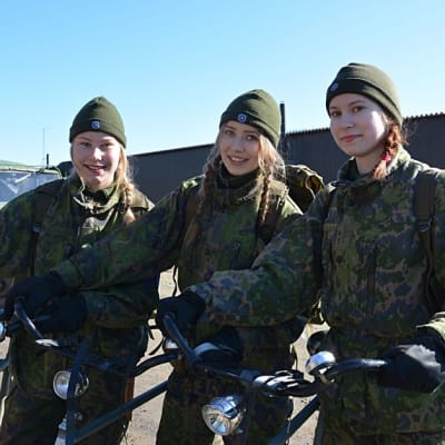 Kolme lukiolaistyttöä polkupyörineen maastopuvuissa