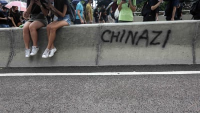 Demonstranter sitter på en betongmur som målats med texten Chinazi.