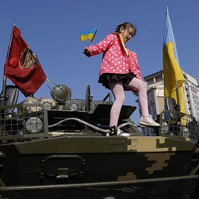 Tyttö leikkii panssarivaunun päällä Ukrainan lippu kädessään.