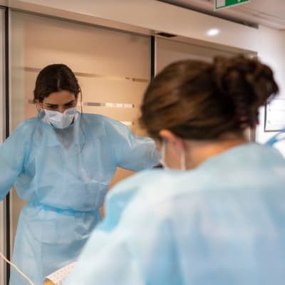 Två sjukskötare i munskydd står och pratar med varandra på ett sjukhus.