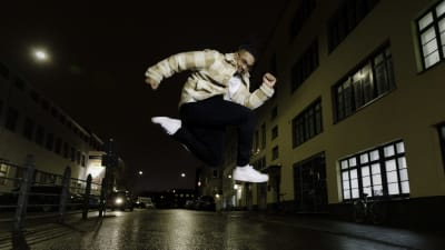 Dansaren Julian Owusu hoppar upp i luften på en tom, nattlig gata.