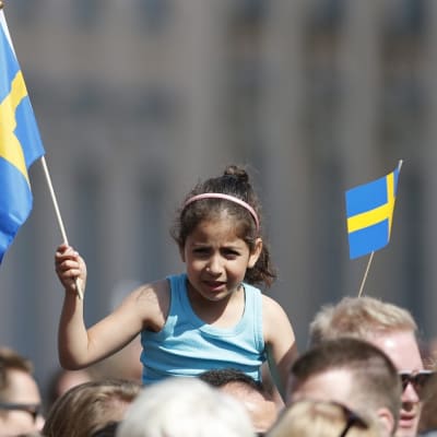 Pikkutyttö istuu aikuisen harteilla ja heiluttaa Ruotsin lippua. 