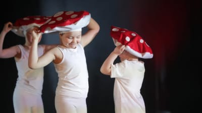 Tre barn dansar och föreställer flugsvampar.